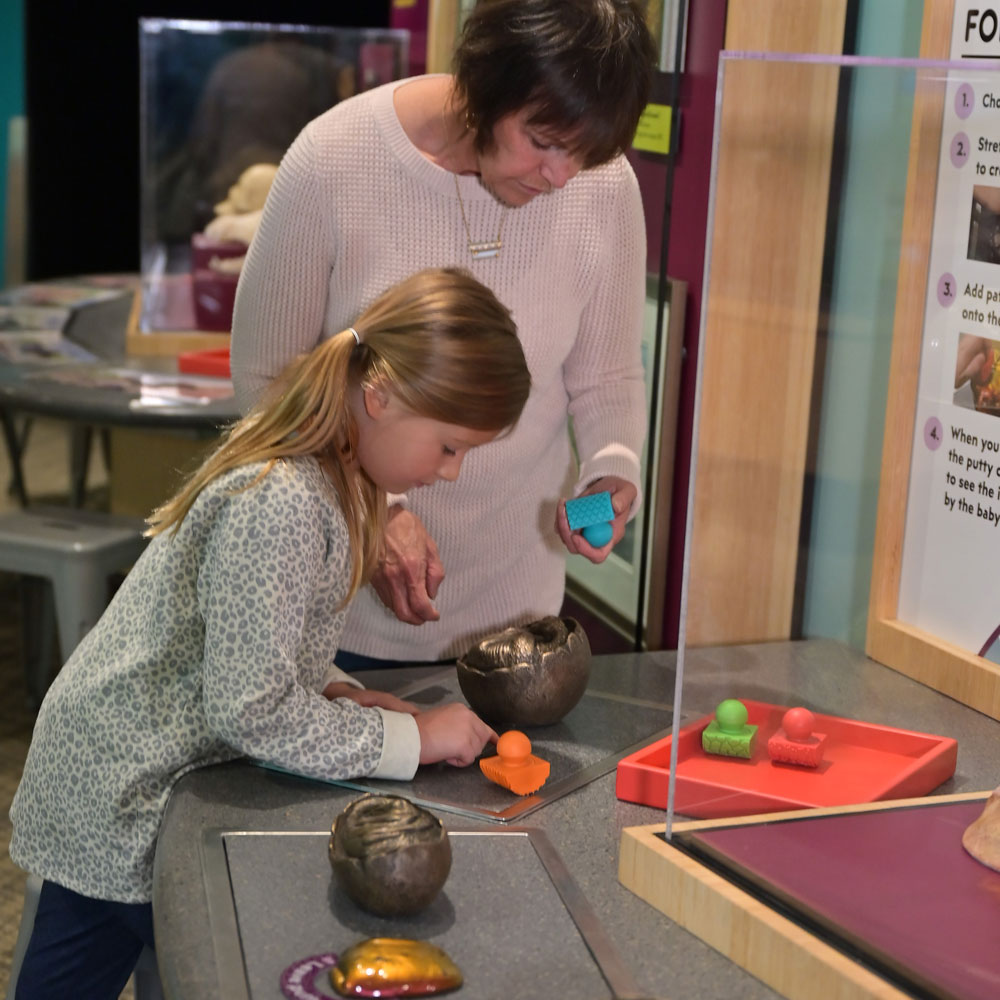 Grown-up and child putting pieces of a putty-like substance on incomplete egg sculpture.